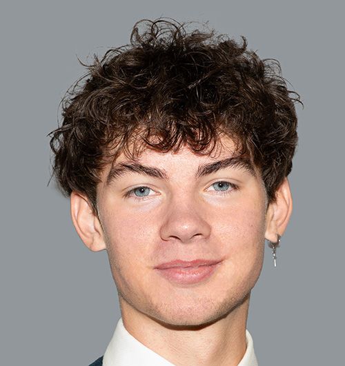 Porträt eines jungen Mannes mit lockigem braunem Haar und silbernem Ohrring vor grauem Hintergrund