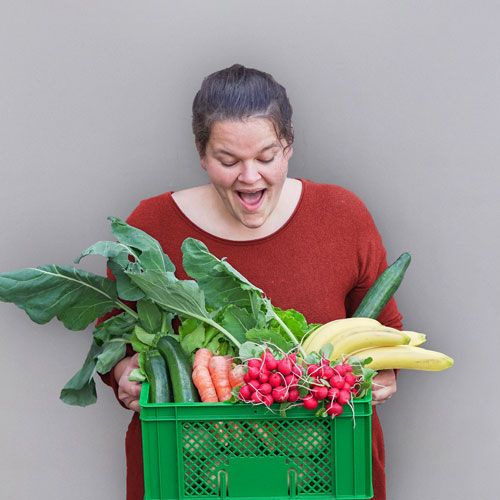 Frau hält Kiste mit frischem Gemüse und Obst und schaut überrascht darauf
