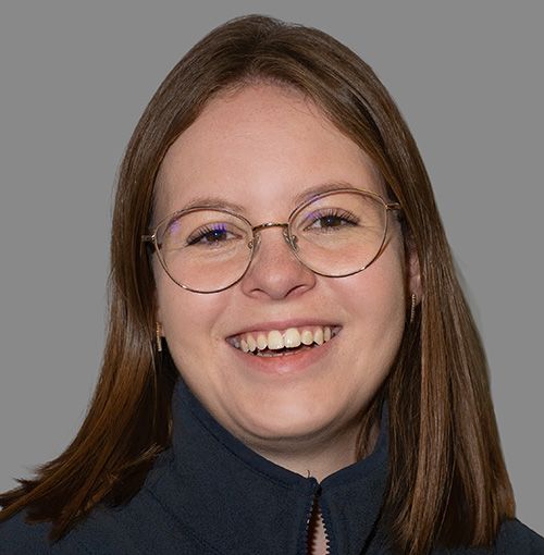 Lächende junge Frau mit Brille vor grauem Hintergrund