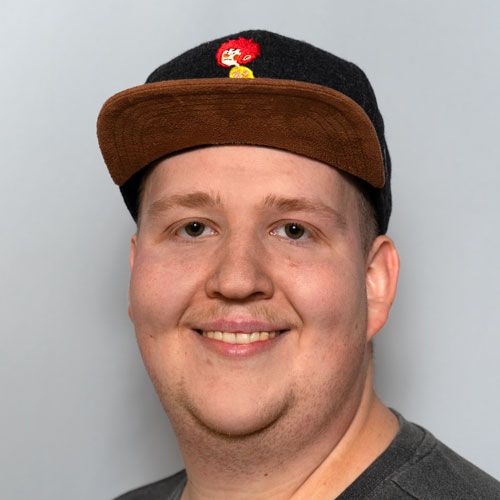 Lächelnder Mann mit schwarzer und brauner Cap vor grauem Hintergrund