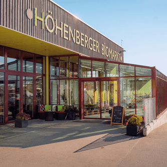 Eingang des Hohenberger Biomarkt mit Glasfassade und Pflanzen vor dem Markt